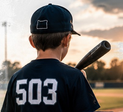 Young player in a 503 jersey holding a bat at sunset